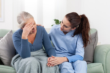 Caring young nurse or doctor comforts an senior woman patient who is upset, stressed, or worried...