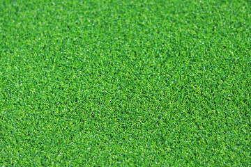 Artificial green grass mat, selective focus. Artificial turf, surface made of synthetic fibers. Green grass texture background. Short artificial grass golf surface