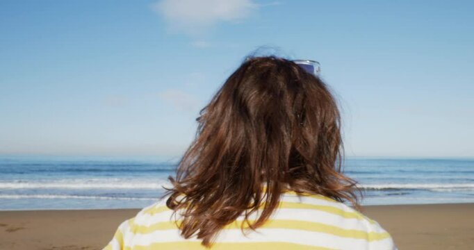 Mujer en la playa frente al mar llama a su perro. Plano desde atr&aacute;s. En un d&iacute;a soleado 