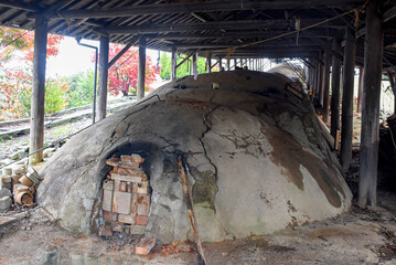 A traditional Japanese noborigama kiln, used for porcelain making, surrounded by rustic wooden beams and vibrant autumn trees, reflecting craftsmanship and history in pottery.
