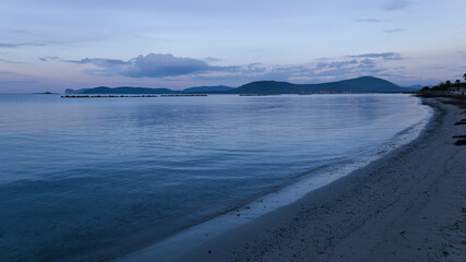 Sunrise on the coast next to the harbor, with the sky illuminated by warm tones. Sardinia