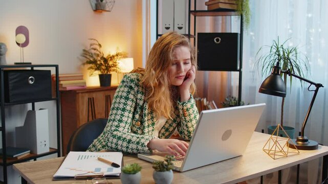 Bored sleepy young blond businesswoman worker working on laptop computer, yawning, leaning on hand at home office desk. Exhausted tired freelancer workaholic girl. Employment, occupation, workless.