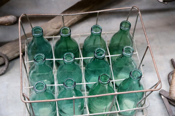 Old green glass bottles in wire basket. Dozen decorative vintage bottles.	
