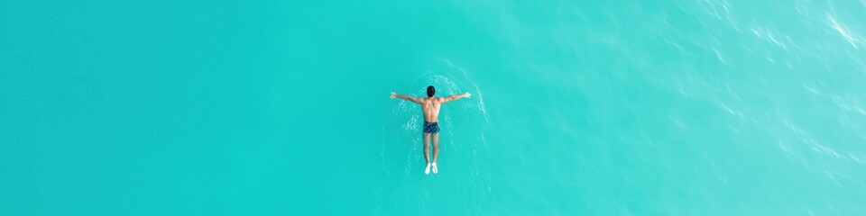 A man is swimming in the ocean. The water is blue and calm. The man is wearing a blue swimsuit