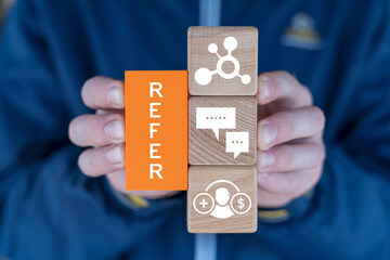 Person holding blocks with icons sees word: REFER. People making money from referral. Refer a friend or referral marketing business concept. Social media marketing for friends.