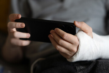 A child with an arm in a cast uses a phone
