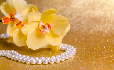 yellow Orchid and pearl necklace on a shiny gold background
