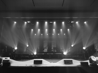 A monochrome view of a stage featuring dramatic spotlights and musical equipment, with a focus on lighting design and ambiance. A timeless, artistic composition.