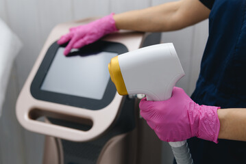 beauty master holds laser hair removal machine in hands, cropped, no face, unrecognizable, pink gloves, young caucasian beautician woman