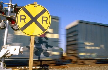 Railroad crossing sign with passing rail cars.  Scanned from film.