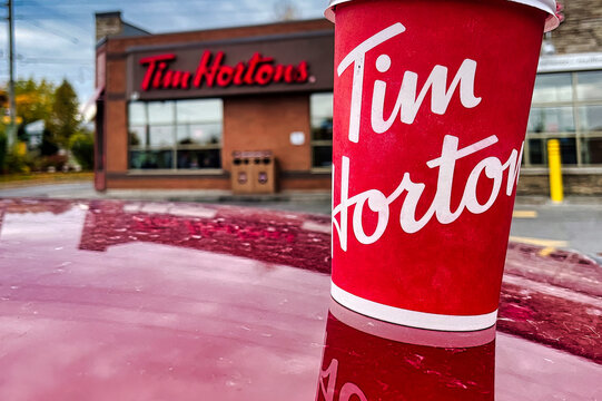 oshawa, canada - 19 October 2022: cup of tim hortons coffee on red car in front of outlet with logo