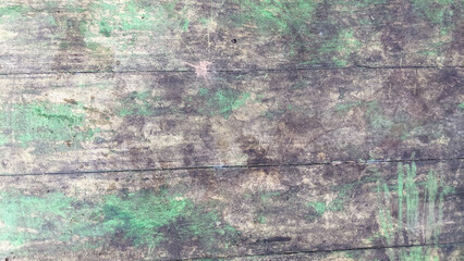 A close-up view of a weathered and worn wooden surface with faded and chipped green paint, revealing the natural wood underneath