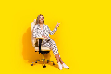 Charming businesswoman in stylish white jacket sits confidently with a smile on yellow background, success and elegance in an office chair.