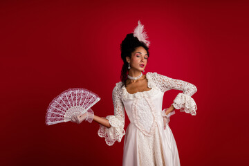 An elegant woman dressed in an ornate white corset gown against a vibrant red backdrop.