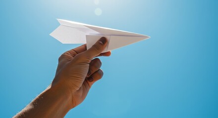 Hand holding paper airplane against clear blue sky for outdoor fun and creativity
