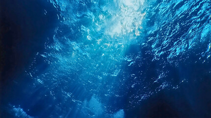 A beautiful image of the bright blue ocean as sunlight pierces through it, the ocean from an underwater perspective with the water gently moving.