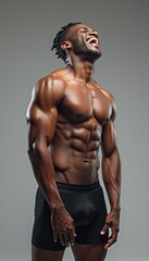 Fototapeta premium A fit, muscular man with a radiant smile stands confidently, showcasing his impressive physique against a neutral gray background. His laughter exudes happiness and vitality, embodying strength and