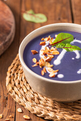 Healthy creamy red cabbage soup topped with herbs, a swirl of cream, toasted almonds, and fresh herbs, resting on a rustic wooden board.