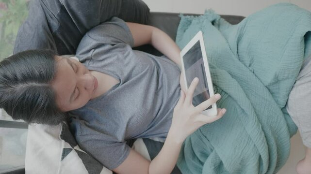 A woman is laying on a couch and using a tablet