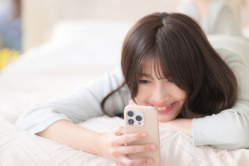 Close-up of a smiling young pretty woman lying on a bed looking at her phone