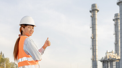Engineer in Safety Gear Gives Thumbs up at Industrial Site With Smokestacks Under a Cloudy Sky