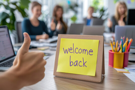 A Team giving thumbs up with welcome back note on desk, celebrating return to work. Positive atmosphere in modern office
