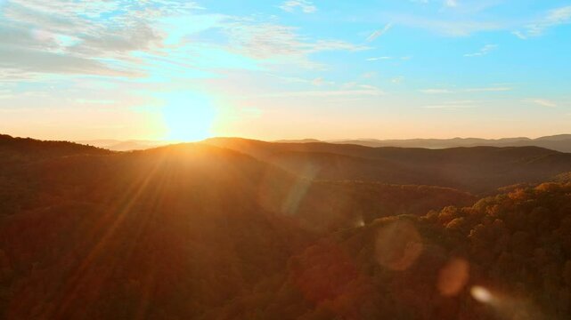 Aerial view of vibrant autumn colors at sunrise in the Blue Ridge Mountains of North Carolina. Panning shot with lens flare.