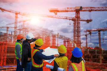 Men and woman meeting with Engineers and supervisors are standing reading the blueprints at the construction site.
