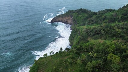 Aerial drone view of coastline with hills and trees, as well as view of coral cliffs and sea with waves from the sea in Menganti Beach Kebumen Central Java Indonesia