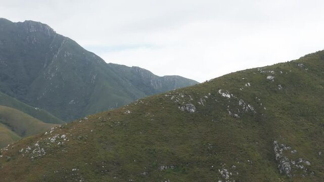 Aerial shot from the peak of an Outeniqua Mountain, Western Cape, South Africa. The drone moves left to reveal more of the majestic mountain range and vast landscape.