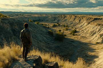Lone man overlooking vast, arid canyon landscape at sunset.