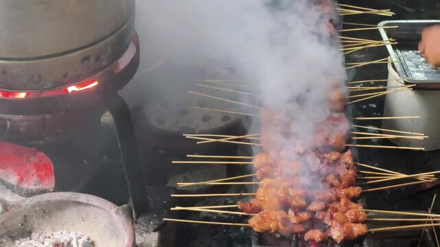 A close-up shot reveals the smoky atmosphere of Beringharjo Market, Yogyakarta, as sate koyor or beef fat satay is grilled over a charcoal fire.