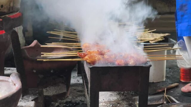 A close-up shot reveals the smoky atmosphere of Beringharjo Market, Yogyakarta, as sate koyor or beef fat satay is grilled over a charcoal fire.