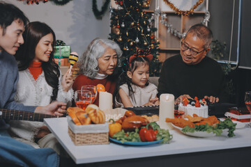 Multi-Generation Family Celebrate Christmas At Home Wearing Santa Hats And Antlers Opening Presents