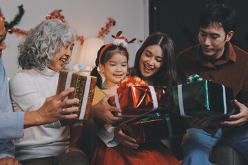 Portrait of Asian family exchanging presents during christmas at home. Attractive happy people holding gift box, celebrate holiday thanksgiving, xmas eve tradition in living room in house together.