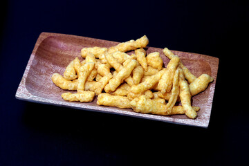 Cheese Puff Snacks on a wooden plate isolated on black background
