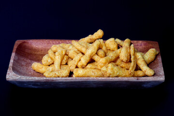 Cheese Puff Snacks on a wooden plate isolated on black background
