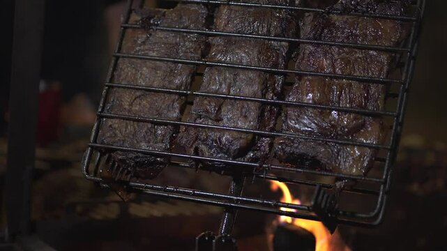 Grilling pieces of meat on a barbecue in patagonia, Argentina, with vibrant flames dancing below, creates an authentic and delicious culinary experience in the outdoors, slow motion reveal