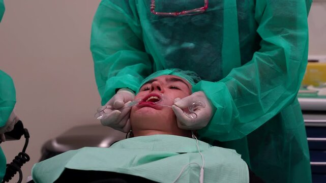 Dentist assistant keeping patient's mouth open with a mouth retractor while odontologist work