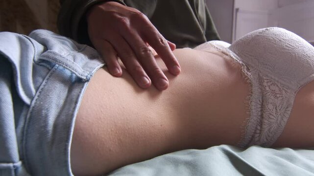 Man gently touching the belly of his girlfriend lying in bra