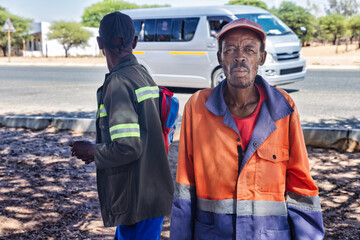 african village township, two workers waiting at the bus stop station, late afternoon, wearing workwear and a hat