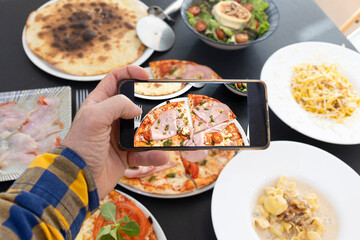Man taking cell phone picture of pizza on table