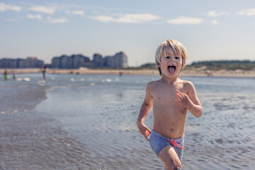 Happy boy running through shallow waves on the beach.