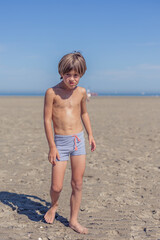 Confident Boy Strolling Across a Sandy Beach Under Sunshine