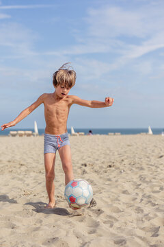 Young Boy Playing Football on a Sandy Beach Day
