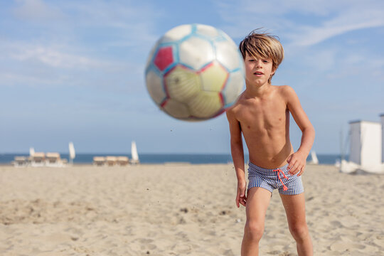 Focused boy skillfully playing soccer on sandy beach scene.
