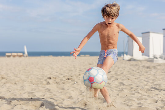 Young boy playing soccer on sandy beach with determination.