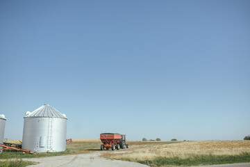 Farm silo, tractor, and trailer by harvested field in Illinois © Cavan