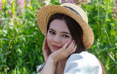 Portrait of a brunette girl in a straw hat outdoors in summer