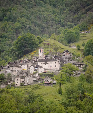 Old mid-century town full of stone houses, a church and a yellow car on a forest covered mountain side, Corippo, Switzerland